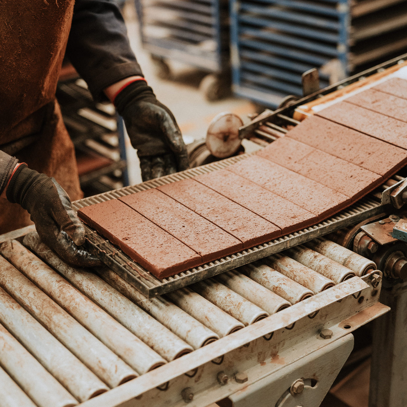 Craftsperson handling freshly cut Bison Brick ceramic tiles on a factory conveyor during the manufacturing process.
