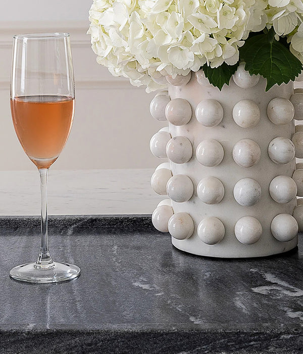 Two glasses of rose wine sit on a dark marble tray beside a textured white marble vase filled with white hydrangeas.